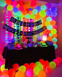 a birthday party with neon colored balloons and streamers on the wall, along with a black table cloth that says glow have happy birthday