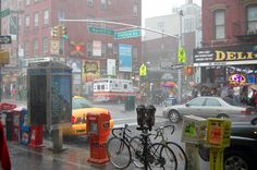 a city street filled with traffic next to tall buildings and parked cars on a rainy day