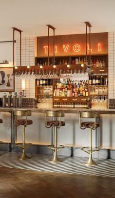 a bar with stools and bottles on the back wall in front of an illuminated sign