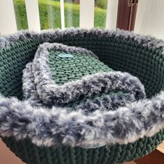 a knitted basket sitting on top of a wooden table next to a window sill