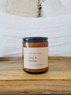 a jar of honey and hazelnut sits on a wooden table in front of a bed