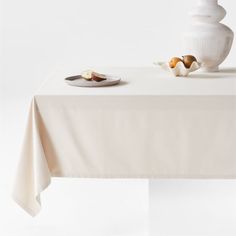 a white vase sitting on top of a table next to a plate with food in it