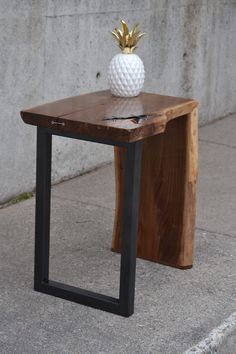 a wooden table with a metal frame and a pineapple on top, sitting in front of a concrete wall