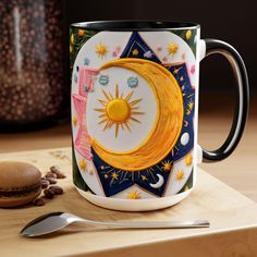 a coffee mug with the sun and moon painted on it, next to a spoon