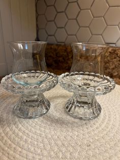 two clear glass vases sitting on top of a white tablecloth covered countertop