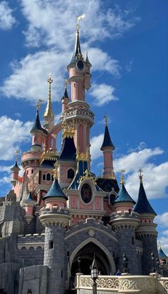 the castle is pink and blue with gold decorations on it's roof, and there are clouds in the sky above