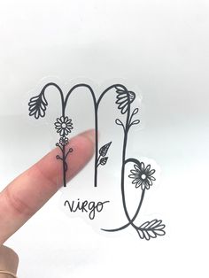 a hand holding up a sticker with the word virgo written in black ink