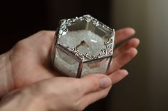 a person holding a ring in their hand with ice on the inside and an empty box behind it