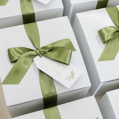 four white boxes with green ribbons and tags on them, all wrapped in satin ribbon