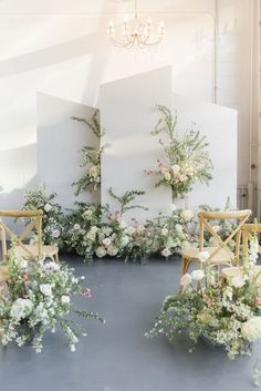 two chairs with flowers and greenery on them in front of a white wall behind them