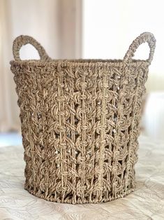 a large woven basket sitting on top of a bed next to a white wall and window