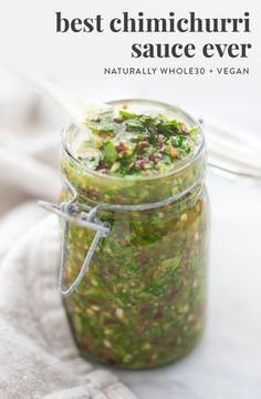 a glass jar filled with green sauce on top of a white cloth next to a spoon