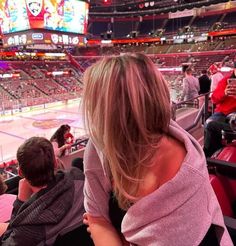 a woman sitting in the stands at a hockey game with her arm wrapped around her neck