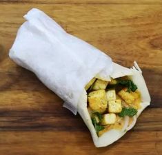 a burrito wrapped in white paper sitting on top of a wooden table