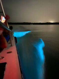 a boat traveling on the water at night with blue light coming from it's side