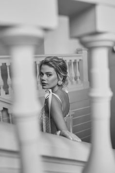 a woman sitting on top of a wooden bench next to white pillars and railings