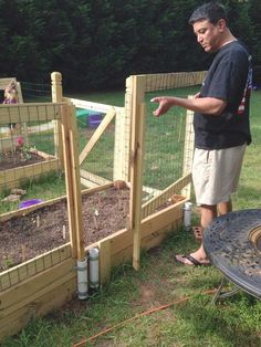 a man standing next to a wooden fence with plants growing in it and another person looking on