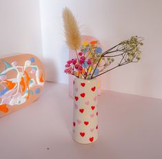 a vase filled with lots of flowers on top of a white table next to a heart shaped box