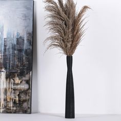 a tall black vase with dry grass in it next to a painting