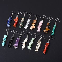 six pairs of earrings with different colored beads and chains hanging from hooks on a black surface