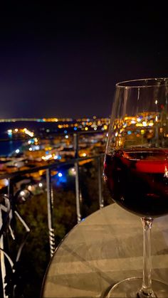 a glass of red wine sitting on top of a table next to a cityscape