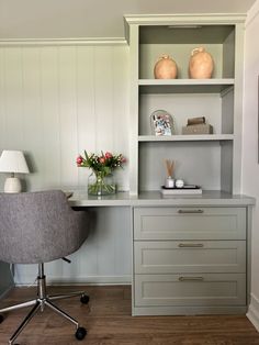 a desk and chair in a room with white paneled walls, wood flooring and open shelving