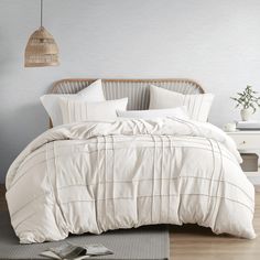 a bed with white comforter and pillows in a room next to a lamp on a table