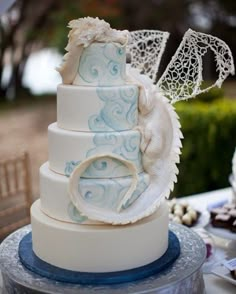 a three tiered wedding cake with blue and white designs on the top, sitting on a table