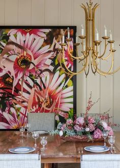 a dining room table with plates and flowers on it in front of a large painting