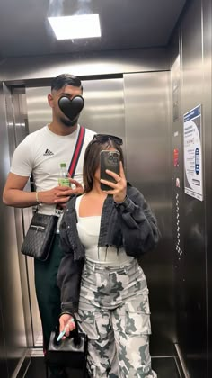 a man taking a selfie in an elevator with a woman holding a cell phone