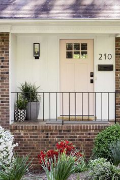 the front door of a brick house with plants and flowers in pots next to it