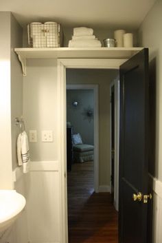 an open door leading to a bathroom with wood floors and white walls, in front of a sink