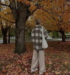 a woman standing in front of a tree with leaves on the ground