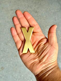 a person's hand holding a gold x brooch in the shape of a letter