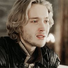 a man with long hair wearing a leather jacket and looking off into the distance while sitting at a table