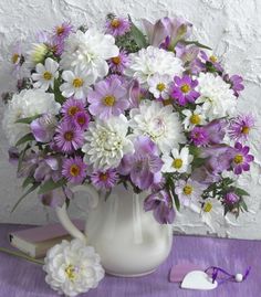 a white pitcher filled with purple and white flowers