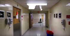 an empty hallway with two red trash cans on the floor and three telephones hanging from the ceiling