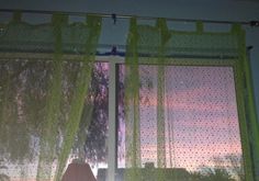 there is a window with green curtains in front of the trees and sky outside it