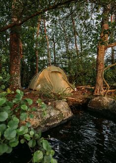 a tent is pitched up in the woods next to a river with rocks and trees