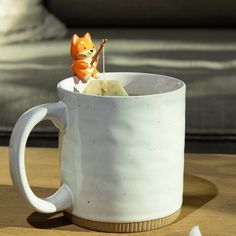 a cat figurine sitting on top of a white coffee cup with toothpicks in it