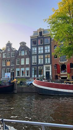 two boats parked on the side of a river next to tall brick buildings and trees