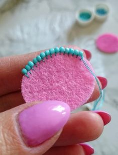 a woman's hand with pink and blue nail polish holding a small piece of felt