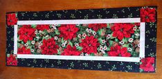 a table runner with poinsettis and pine cones on the border is sitting on a wooden surface