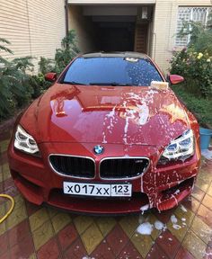 a red car is parked in front of a house with snow on the hood and windows