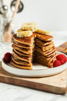 a stack of pancakes on a plate with bananas and raspberries next to it