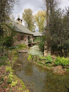 an old stone house with a stream running through it and trees in the foreground