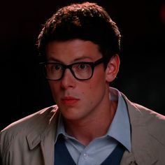 a young man wearing glasses and a blue shirt is staring at something in the distance