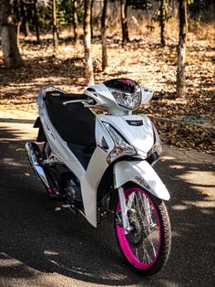 a white and pink motorcycle parked on the side of a road in front of trees