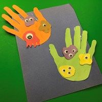 two handprints made to look like hands with faces on them, one is green and the other is orange