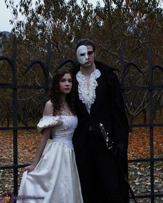 a man and woman dressed up in costume standing next to each other near a fence